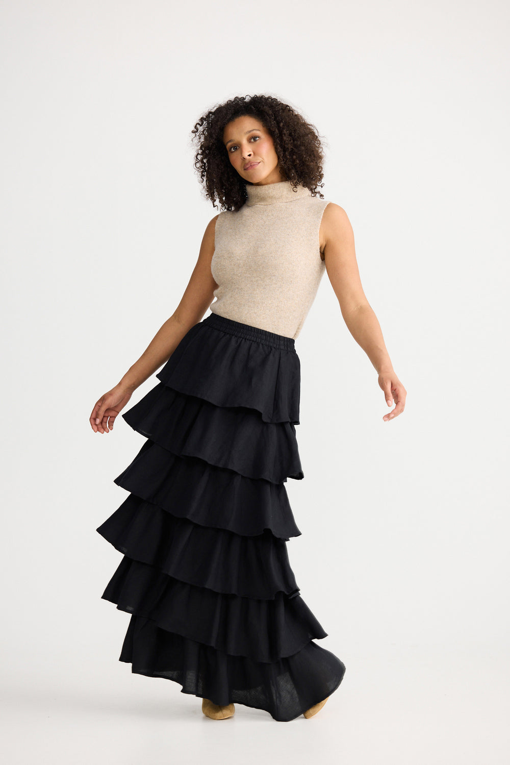 Woman wearing a black tiered skirt and beige top on a white background