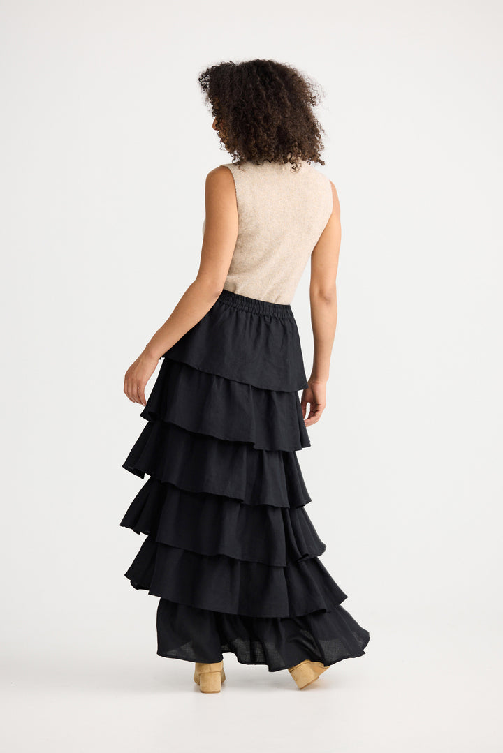 Woman wearing a black tiered skirt and beige top on a white background