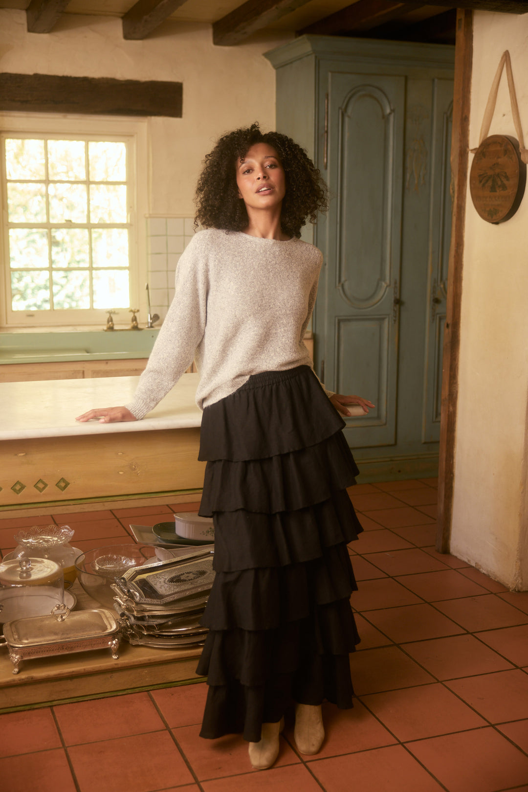 Woman in a kitchen wearing a white sweater and black tiered skirt.