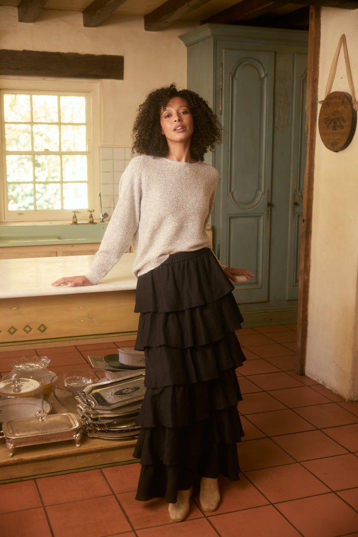 Woman in a kitchen wearing a white sweater and black tiered skirt.