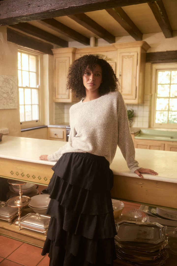 Woman standing in a rustic kitchen with wooden beams and large windows.