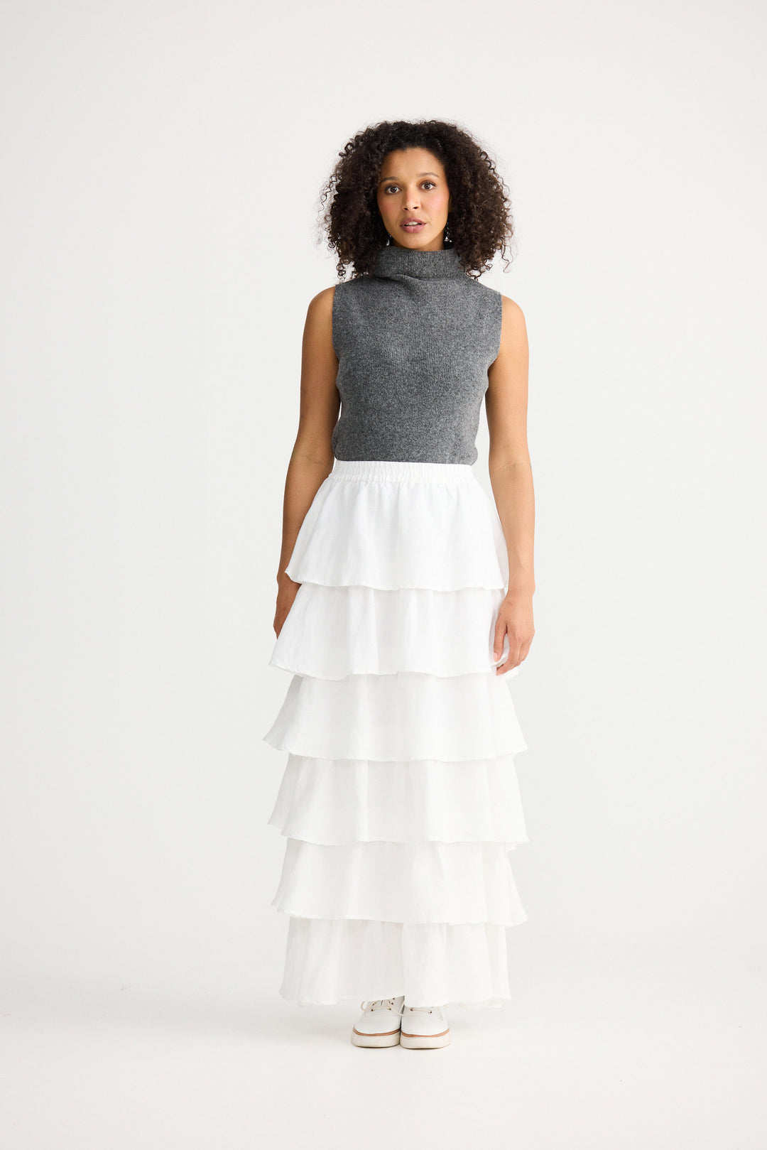 Woman wearing a gray sleeveless top and white tiered skirt on a white background