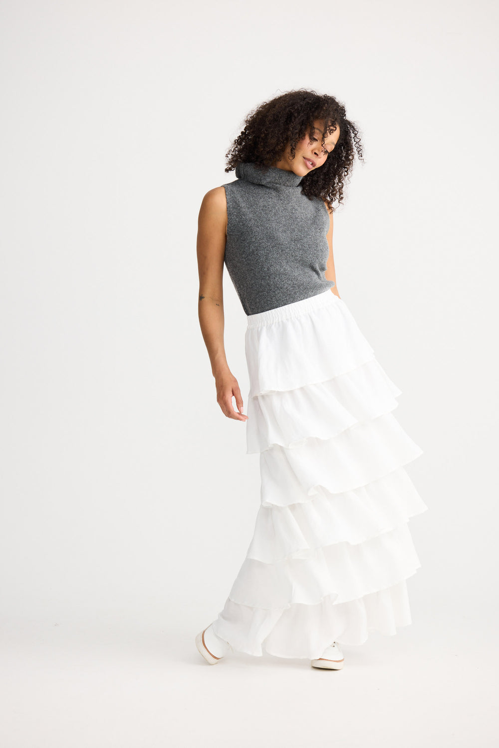 Woman wearing a gray sleeveless top and white pants on a white background