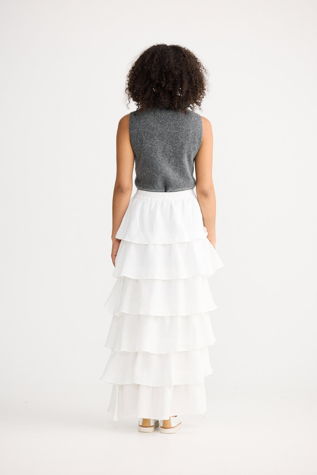 Woman wearing a gray sleeveless top and white tiered skirt on a white background