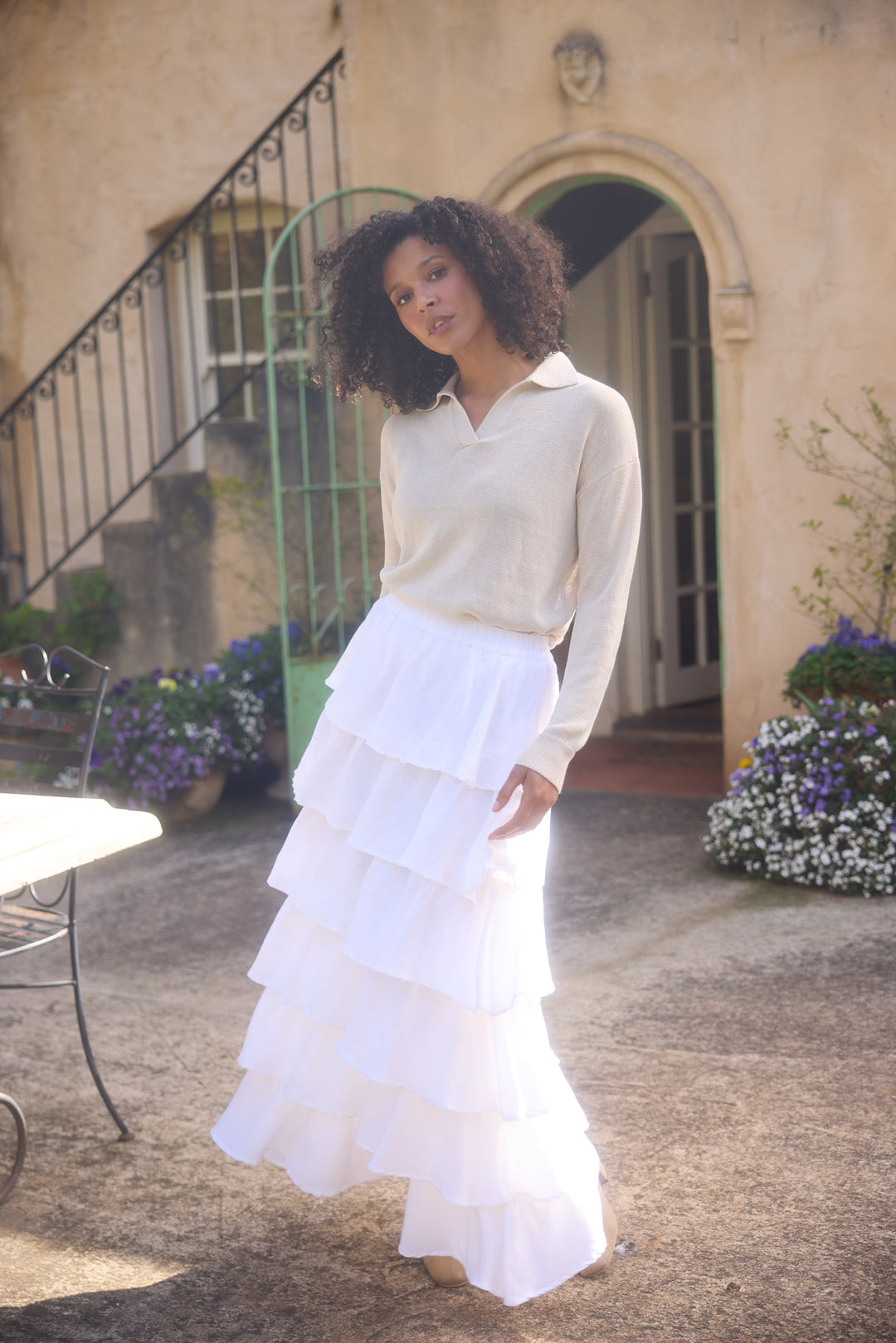 Woman in a white dress standing in front of a building with flowers and a staircase.
