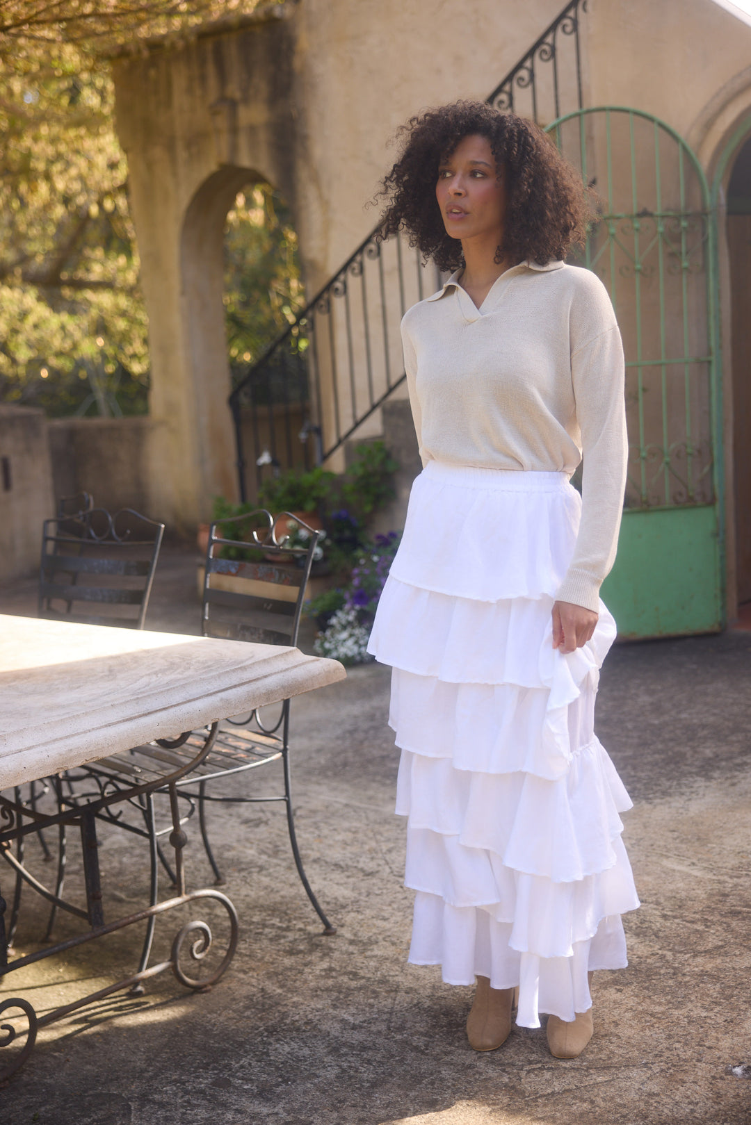 Woman in a white outfit standing outdoors near a table and chairs.