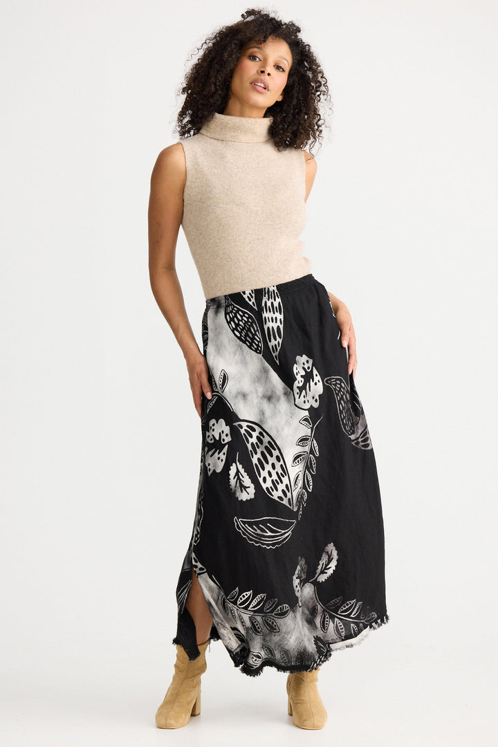 Woman wearing a cream sleeveless top and black patterned skirt on a white background