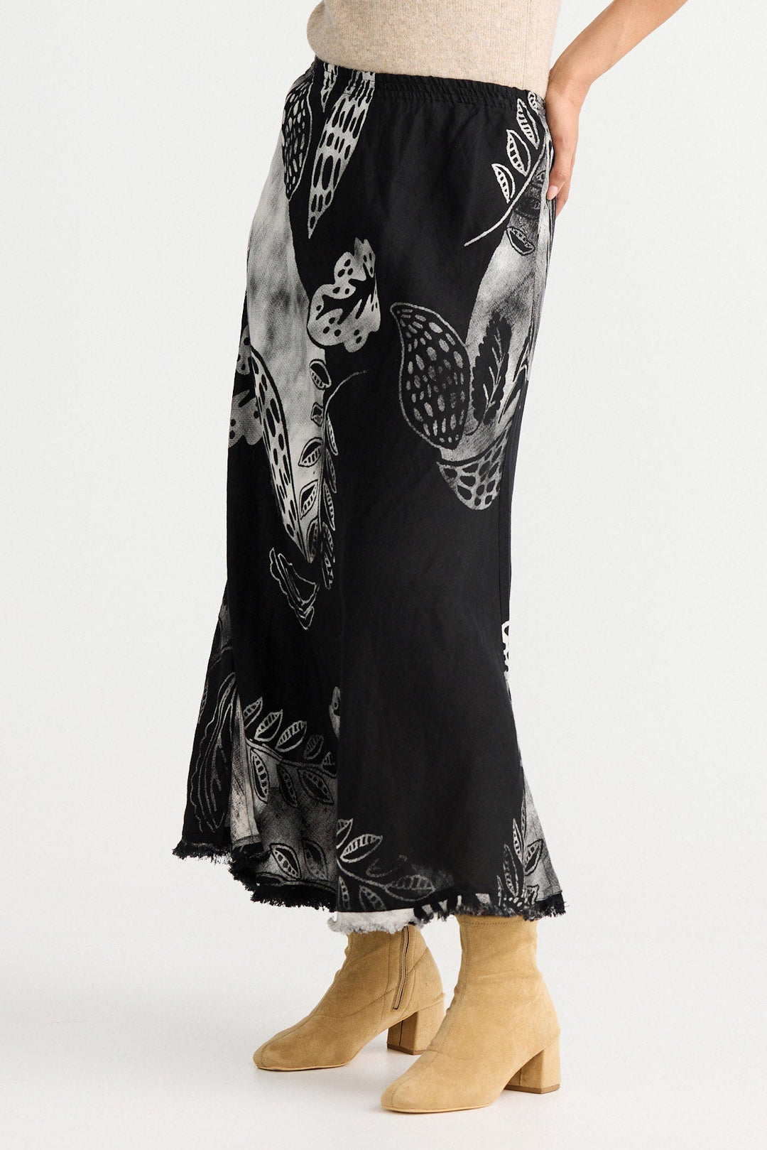 Woman wearing a beige sleeveless top and black floral skirt on a white background