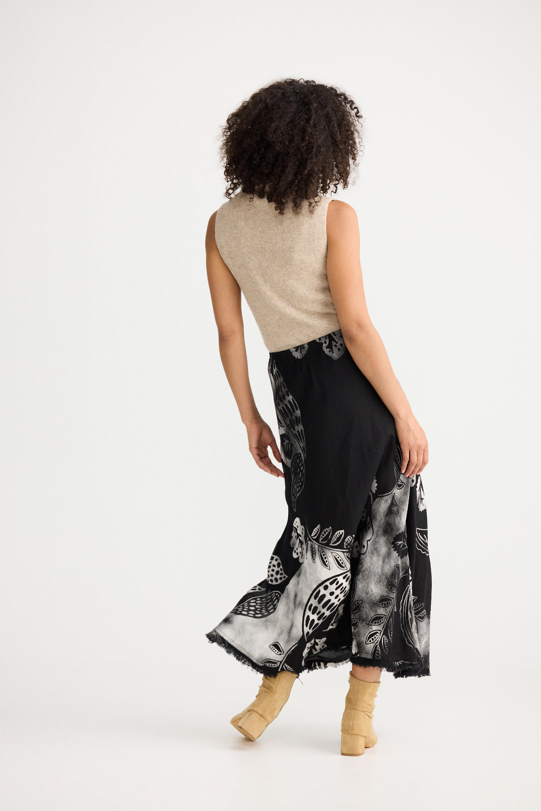 Woman wearing a beige sleeveless top and black patterned skirt on a white background