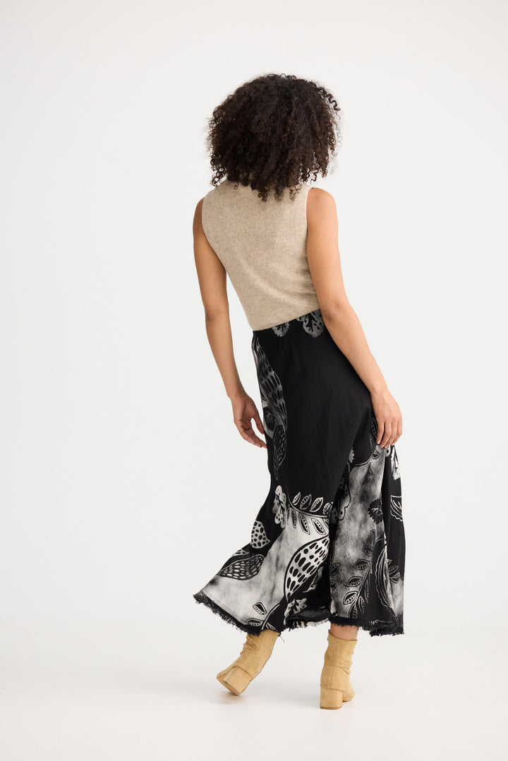 Woman wearing a beige sleeveless top and black patterned skirt on a white background