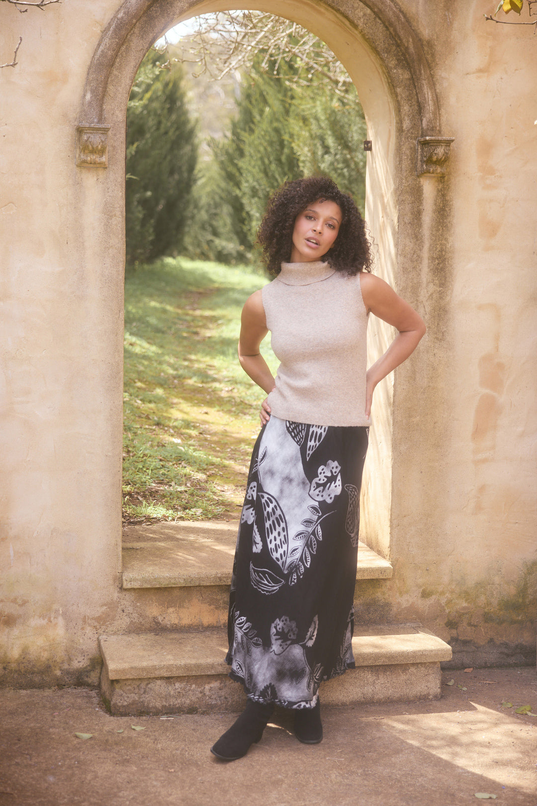 Woman standing in a garden with stone archway