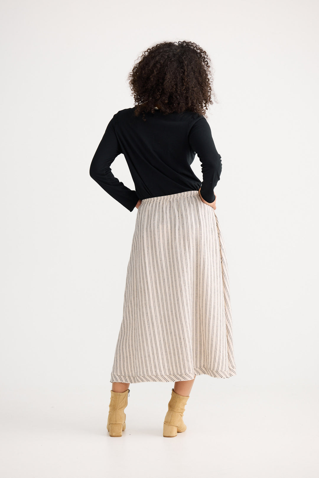 Person wearing a black top and beige pleated skirt on a white background