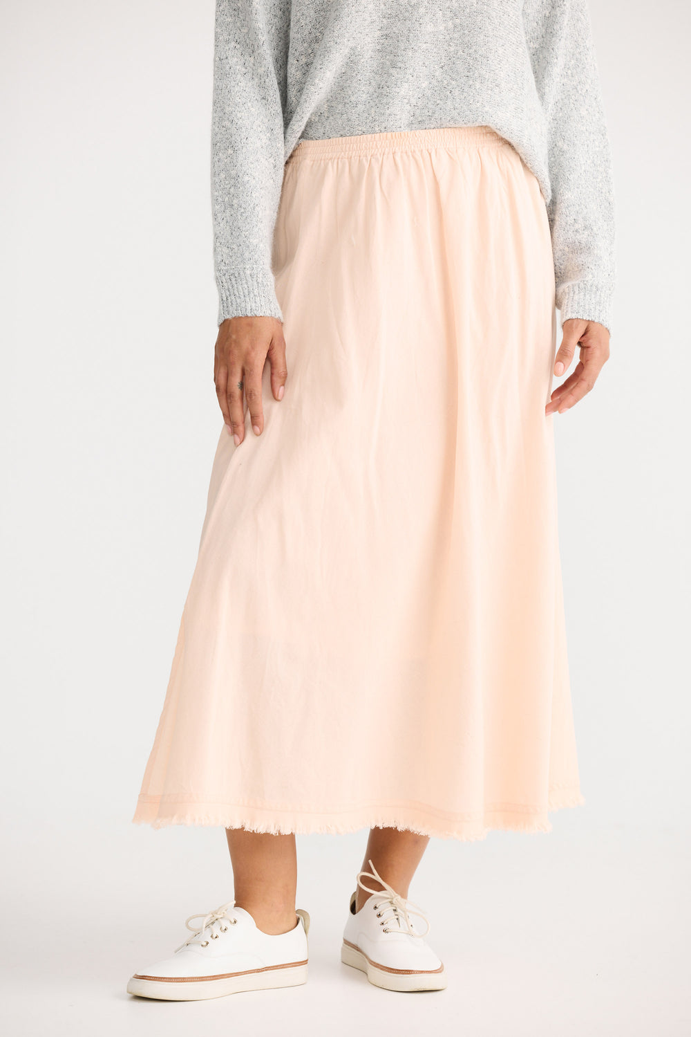 Person wearing a light pink skirt and white sneakers on a plain background