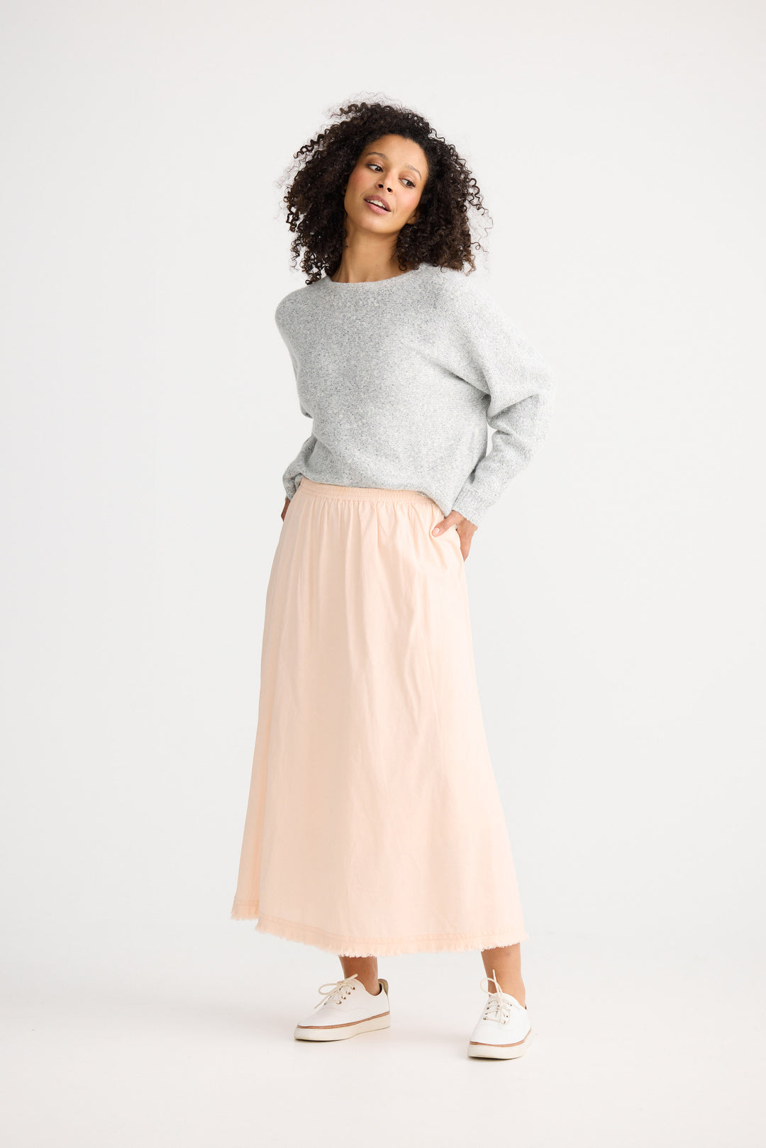 Woman wearing a gray sweater and beige skirt on a white background