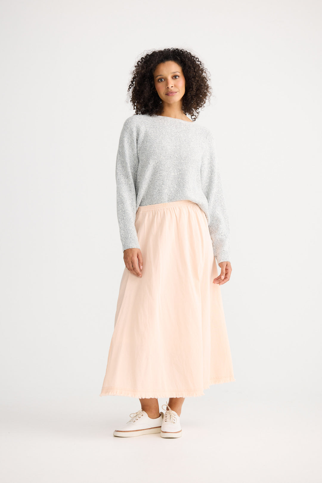 Woman wearing a light gray sweater and pink skirt on a white background