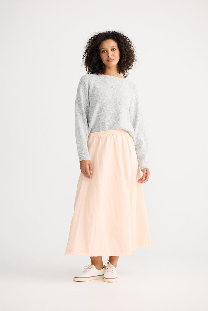 Woman wearing a light gray sweater and pink skirt on a white background
