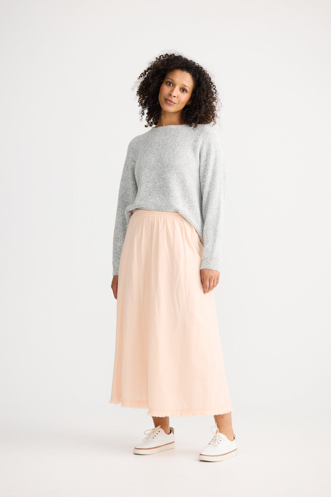 Woman wearing a gray sweater and beige skirt on a white background