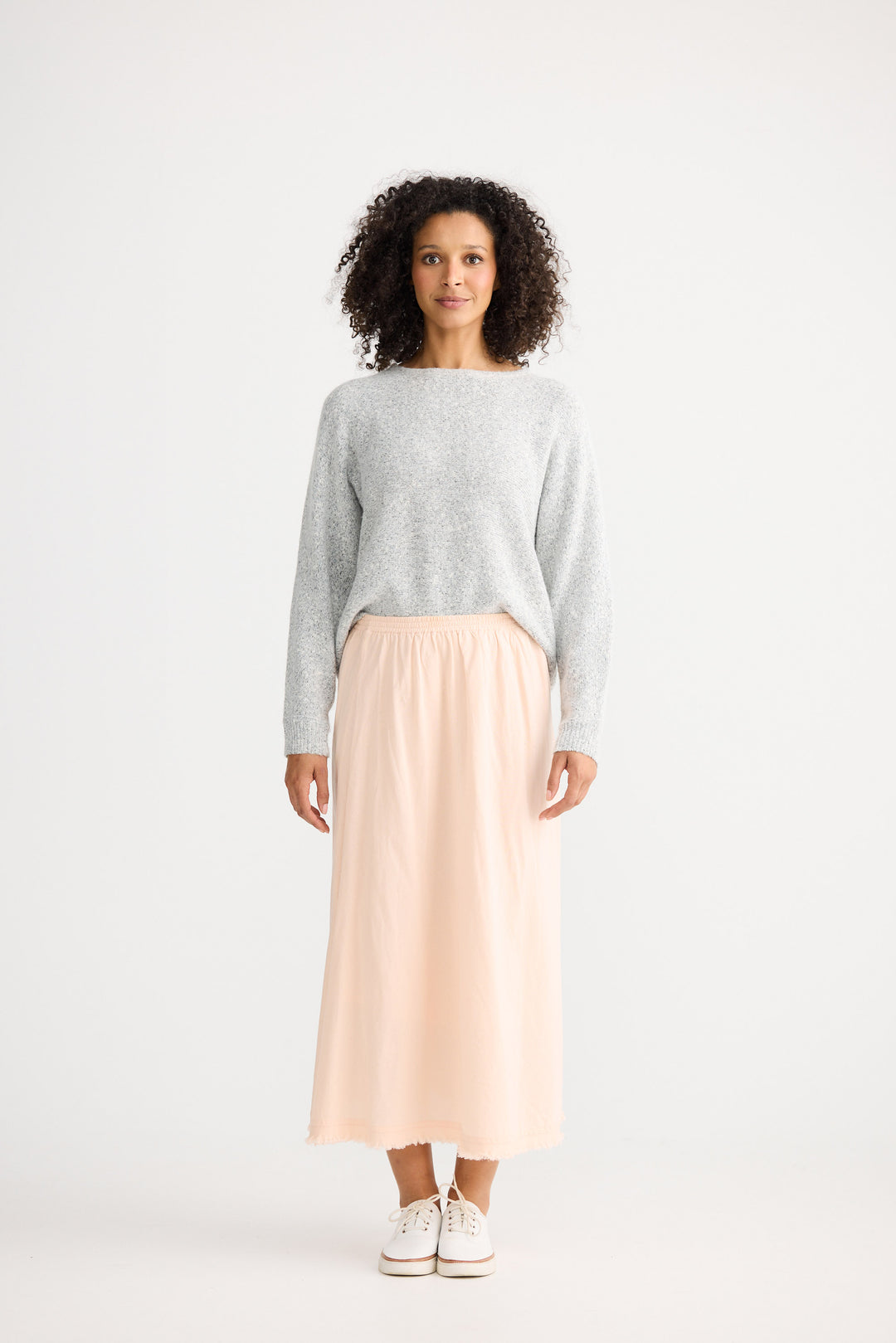 Woman wearing a gray sweater and beige skirt on a white background