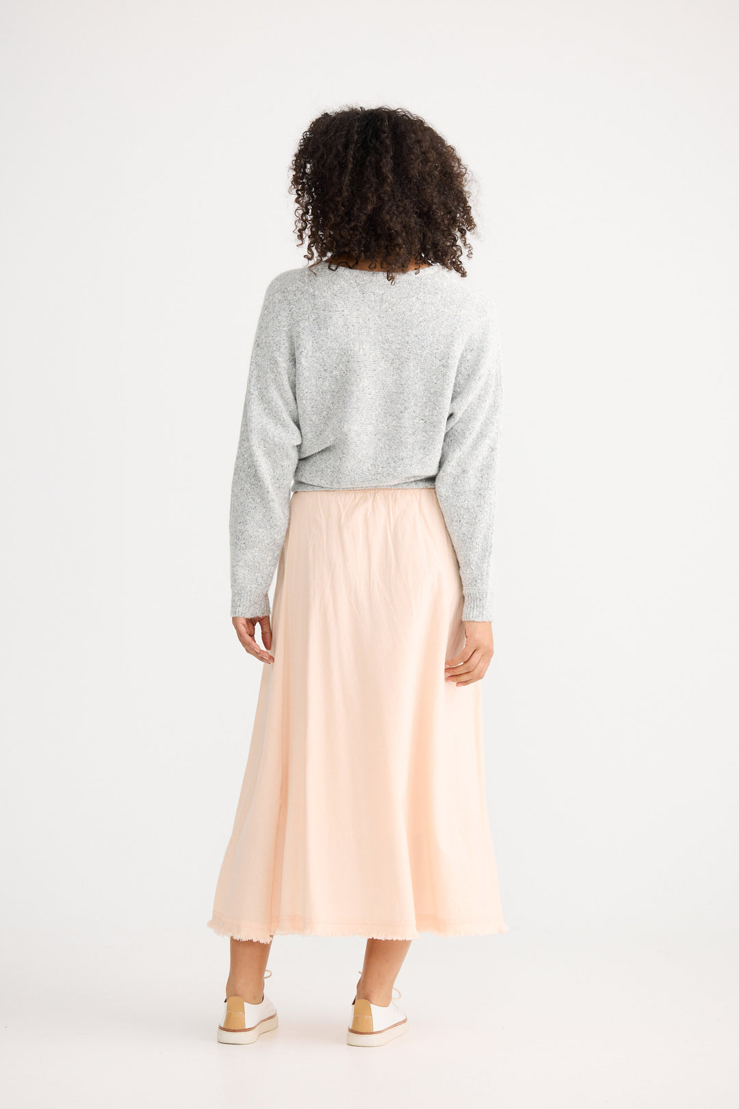 Person wearing a light gray sweater and a long beige skirt on a white background