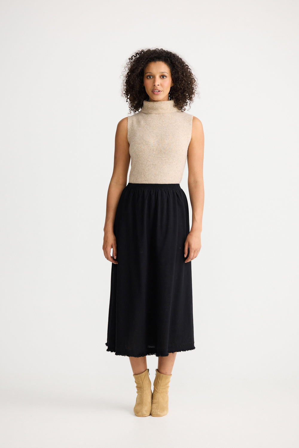 Woman wearing a beige sleeveless top and black skirt on a white background