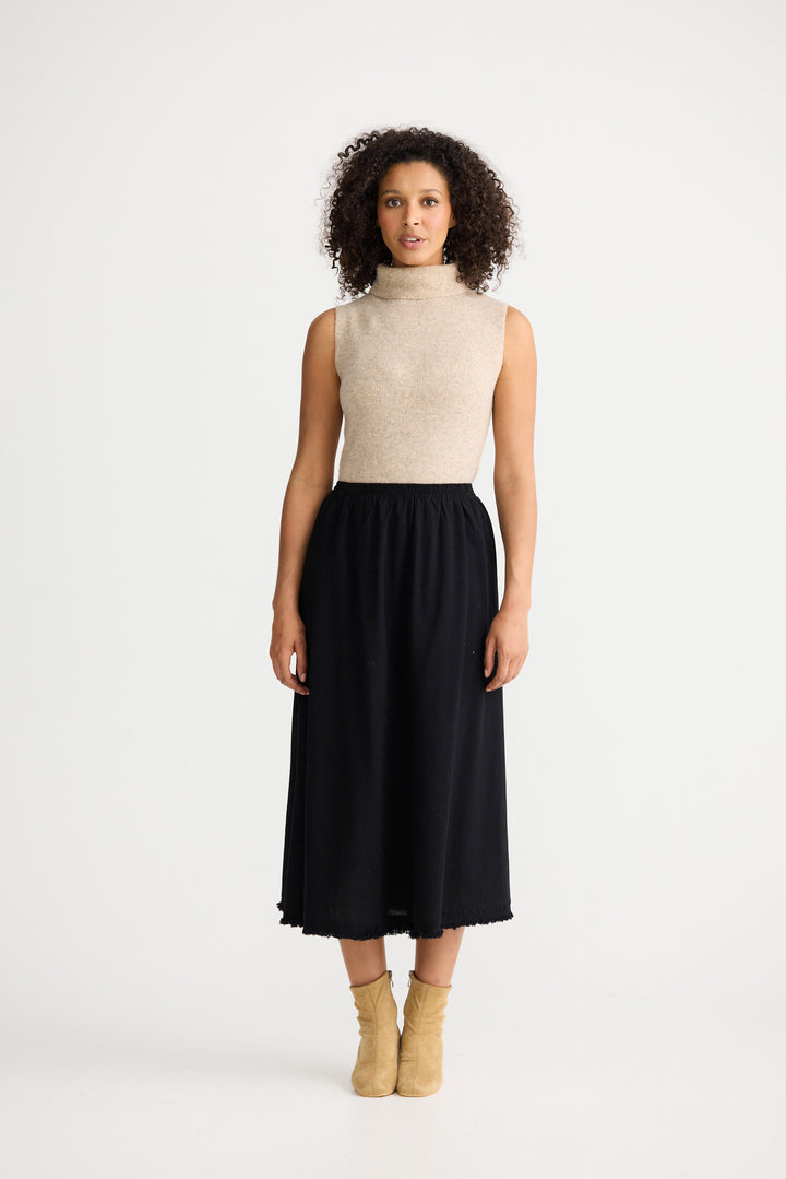 Woman wearing a beige sleeveless top and black skirt on a white background