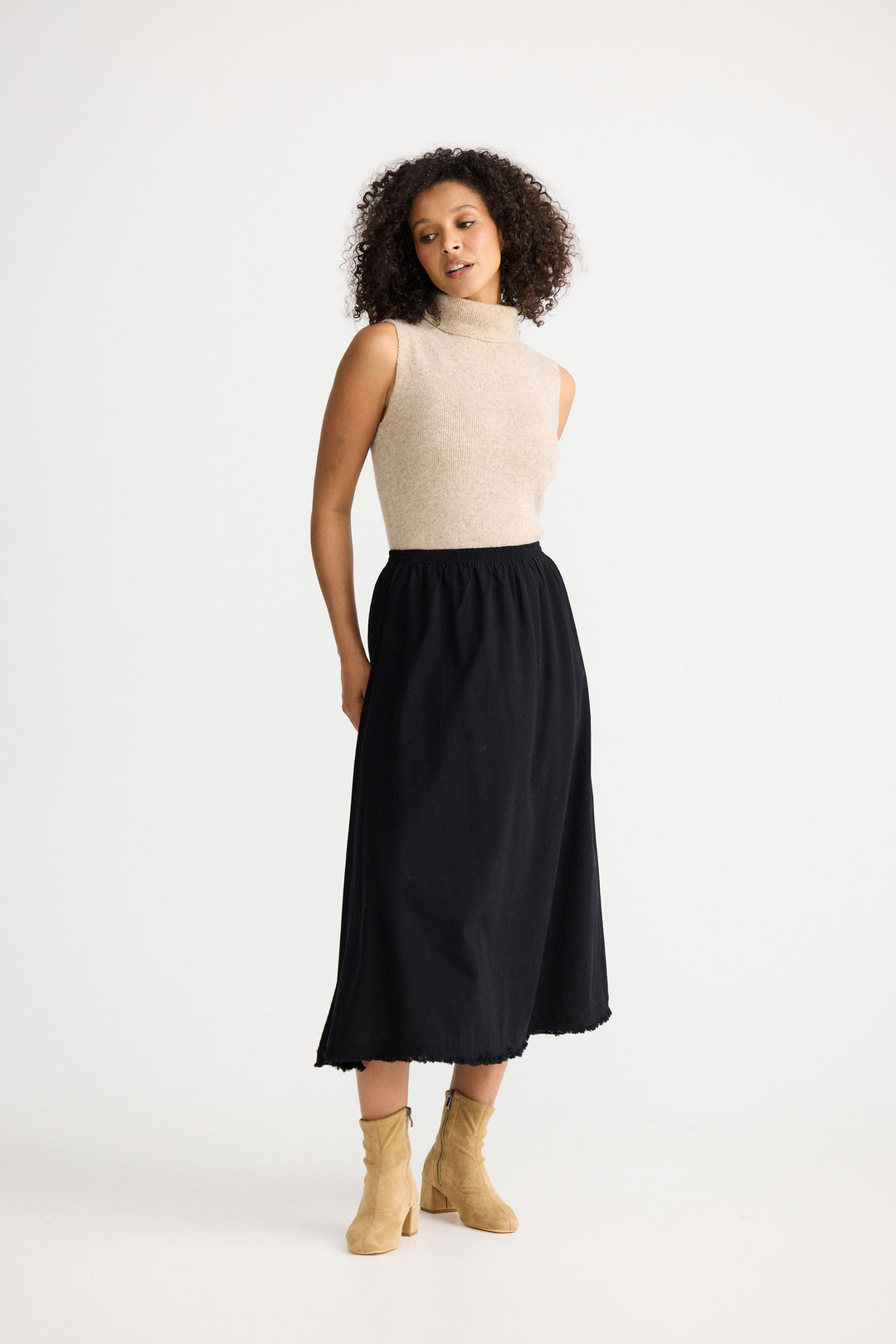 Woman wearing a beige sleeveless top and black skirt on a white background