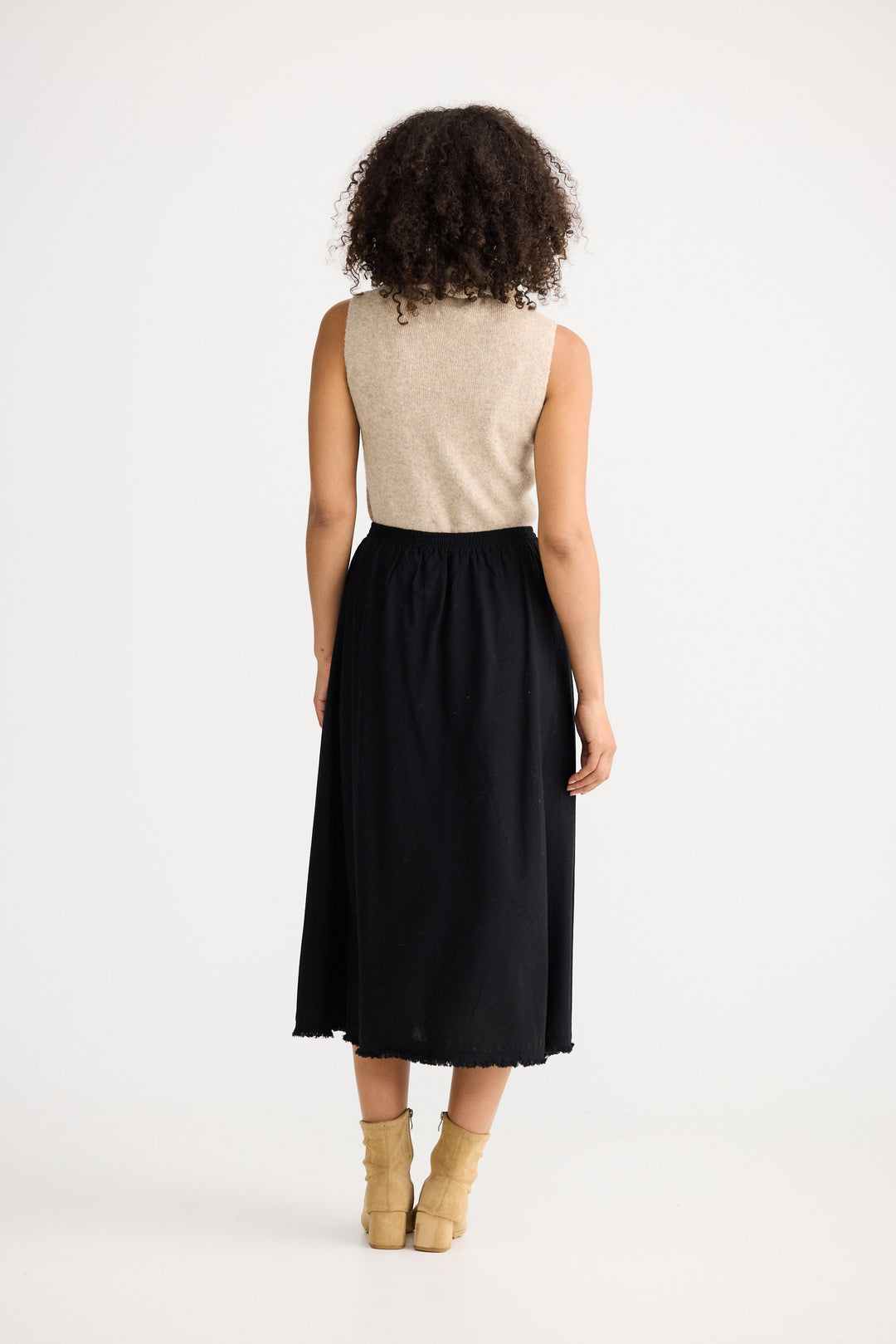 Woman wearing a beige sleeveless top and black skirt on a white background