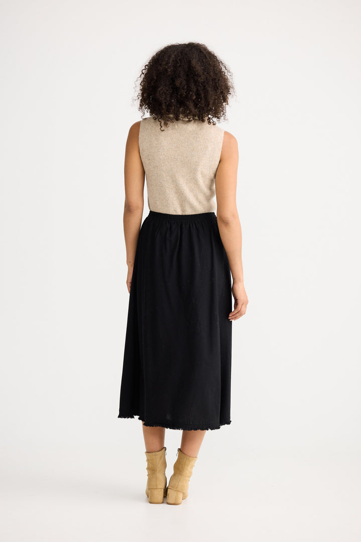 Woman wearing a beige sleeveless top and black skirt on a white background
