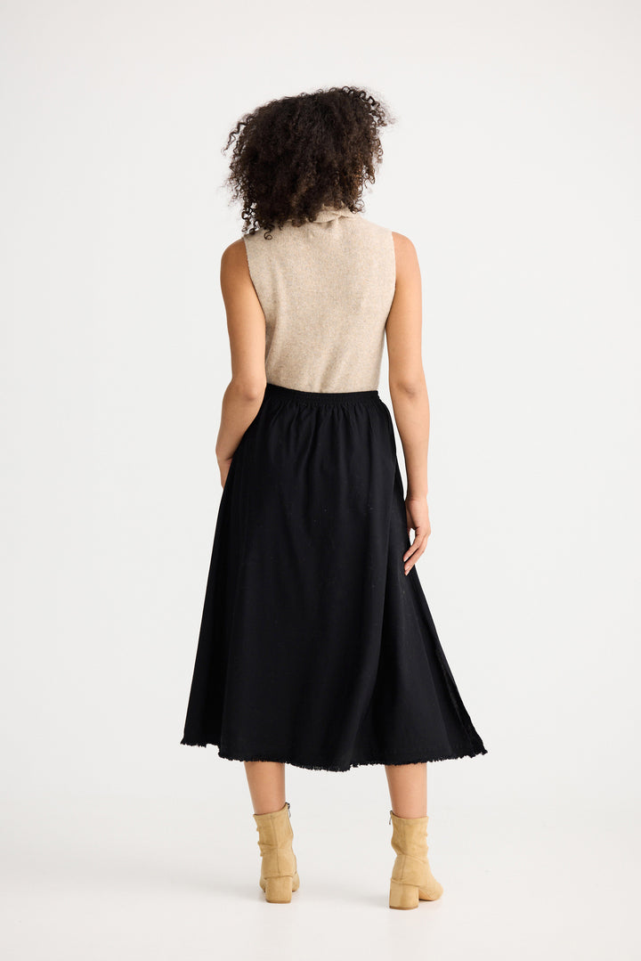 Woman wearing a black skirt and beige top on a white background
