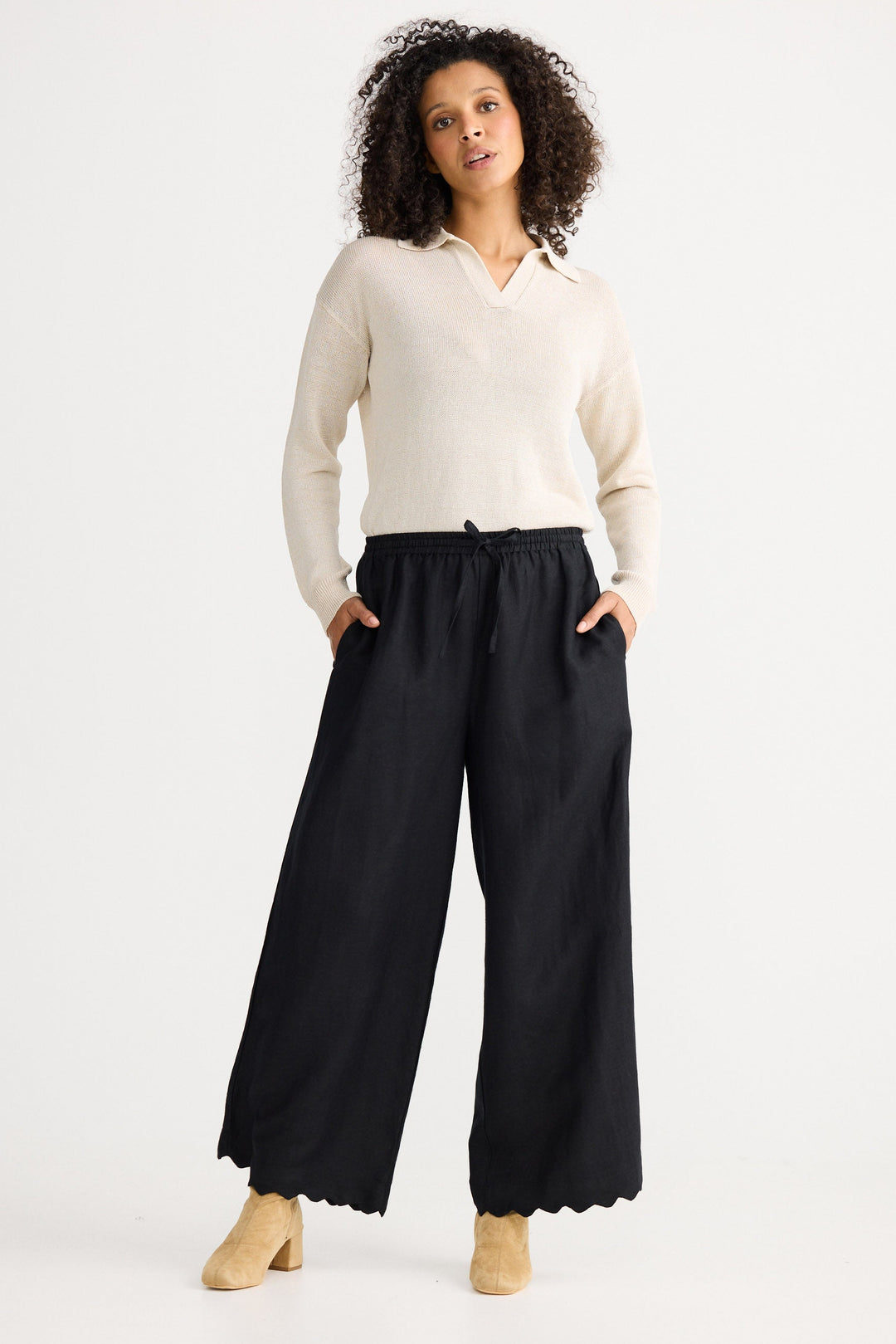 Woman wearing a white sweater and black wide-leg pants on a white background