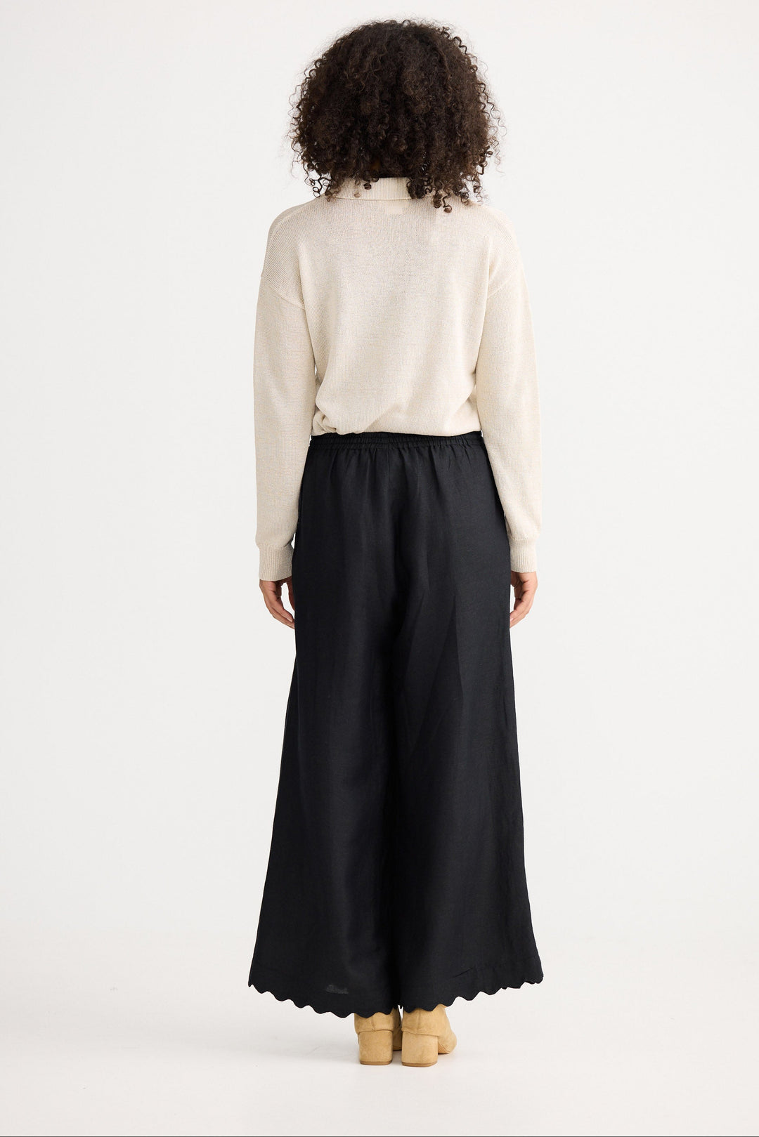 Person wearing a cream sweater and black wide-leg pants on a white background
