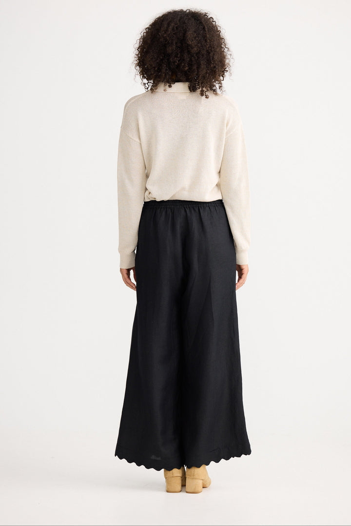 Person wearing a cream sweater and black wide-leg pants on a white background