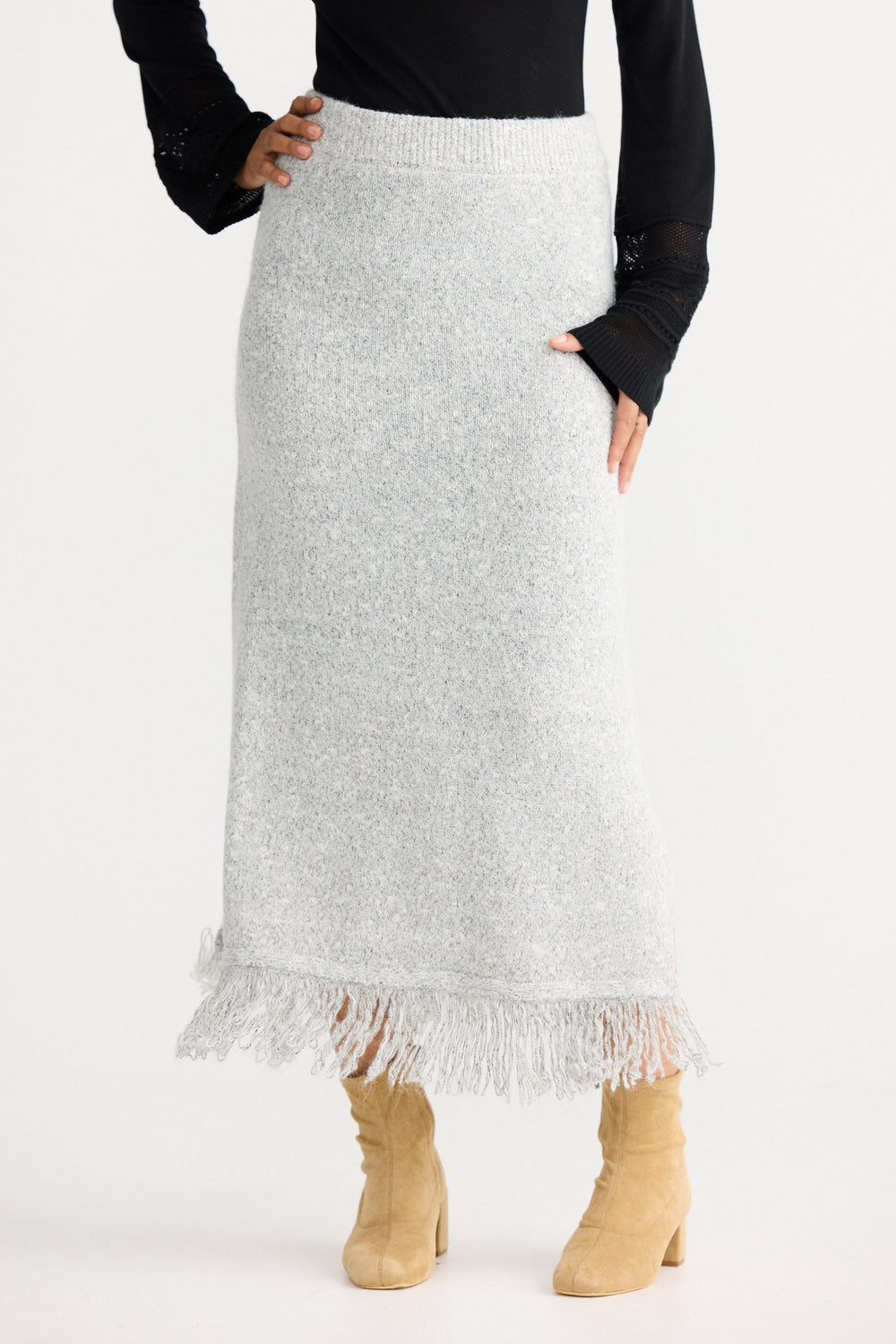 Person wearing a black long-sleeve top and white knit skirt with fringe hem on a white background