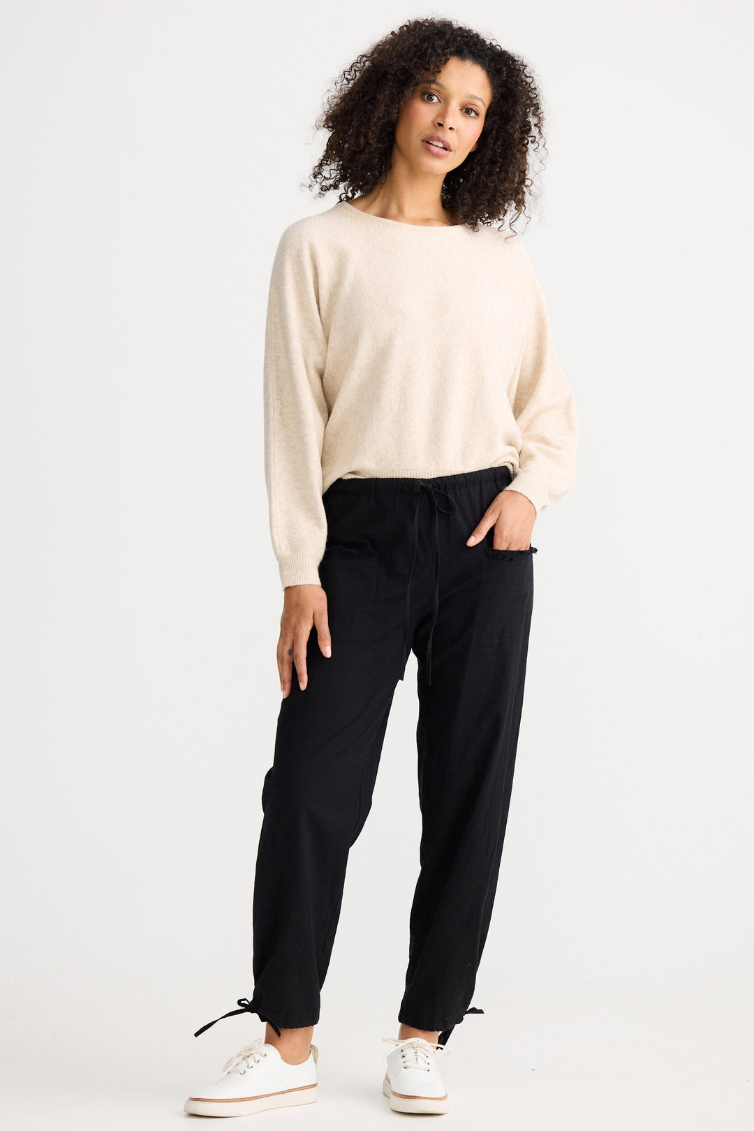 Woman wearing a beige sweater and black pants on a white background
