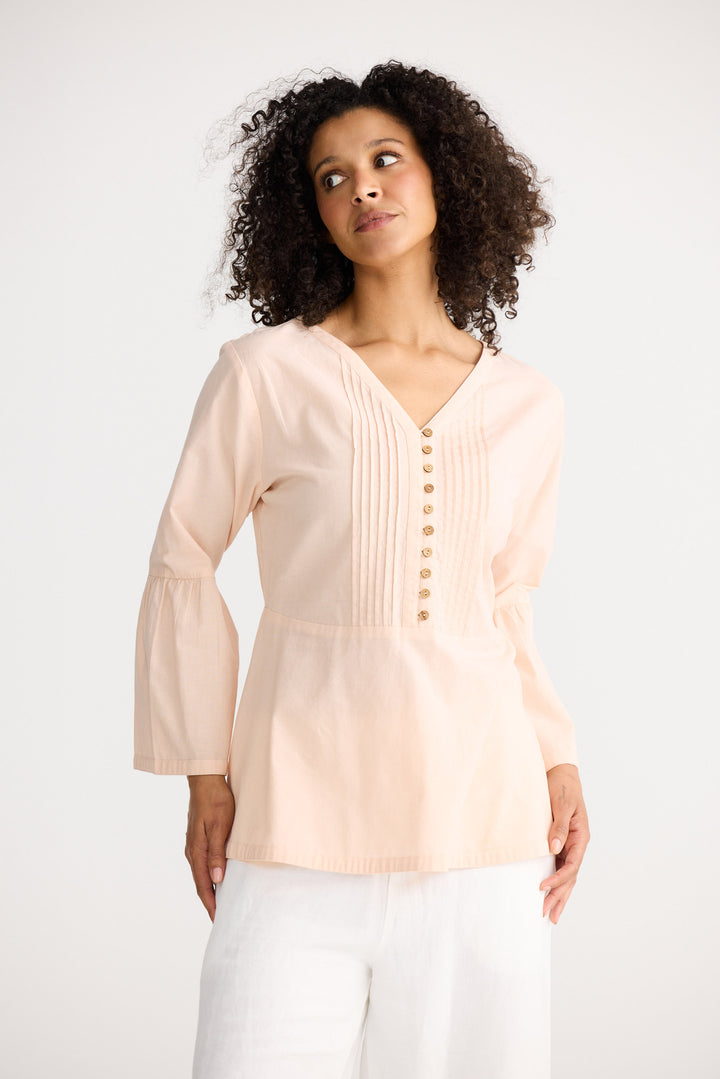 Woman wearing a light pink blouse with bell sleeves on a white background