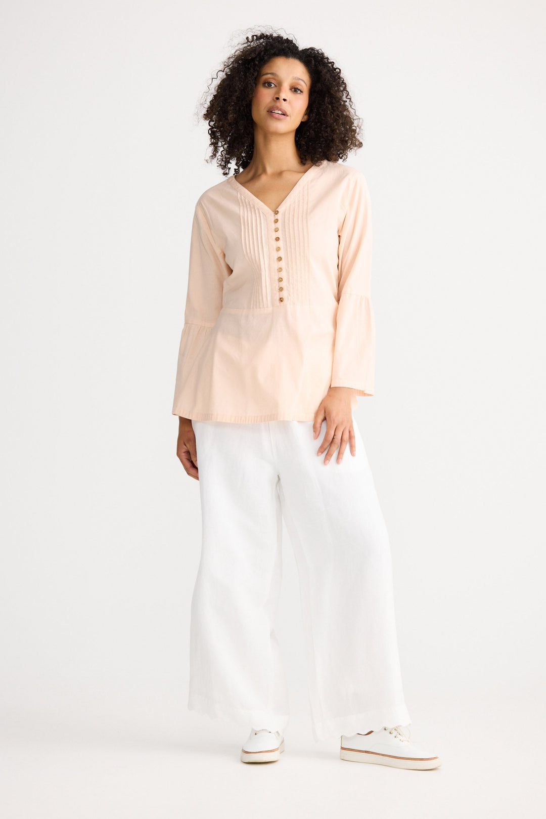 Woman wearing a light pink blouse and white pants on a white background