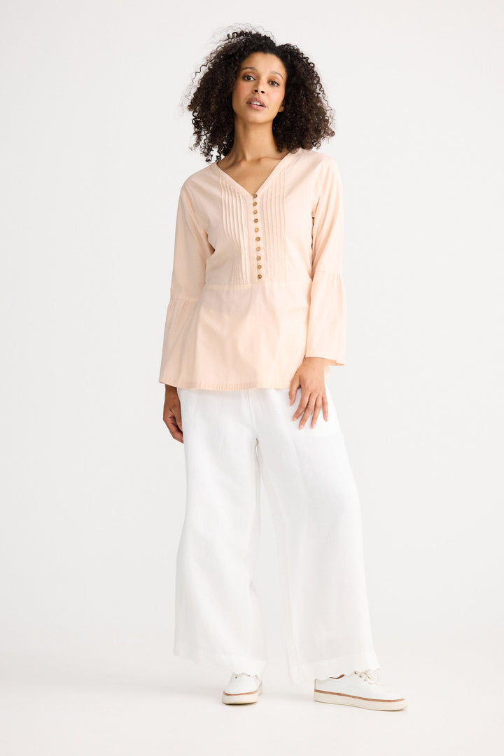 Woman wearing a light pink blouse and white pants on a white background