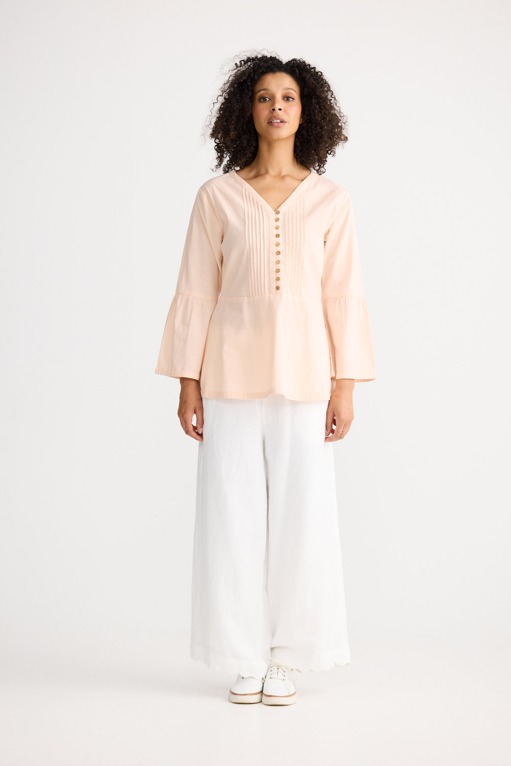 Woman wearing a light pink blouse and white pants on a white background