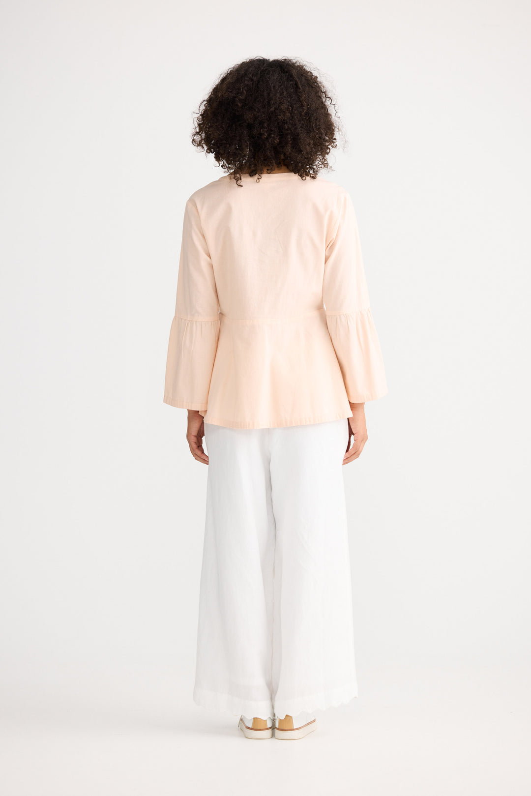 Person wearing a light pink jacket and white pants on a white background