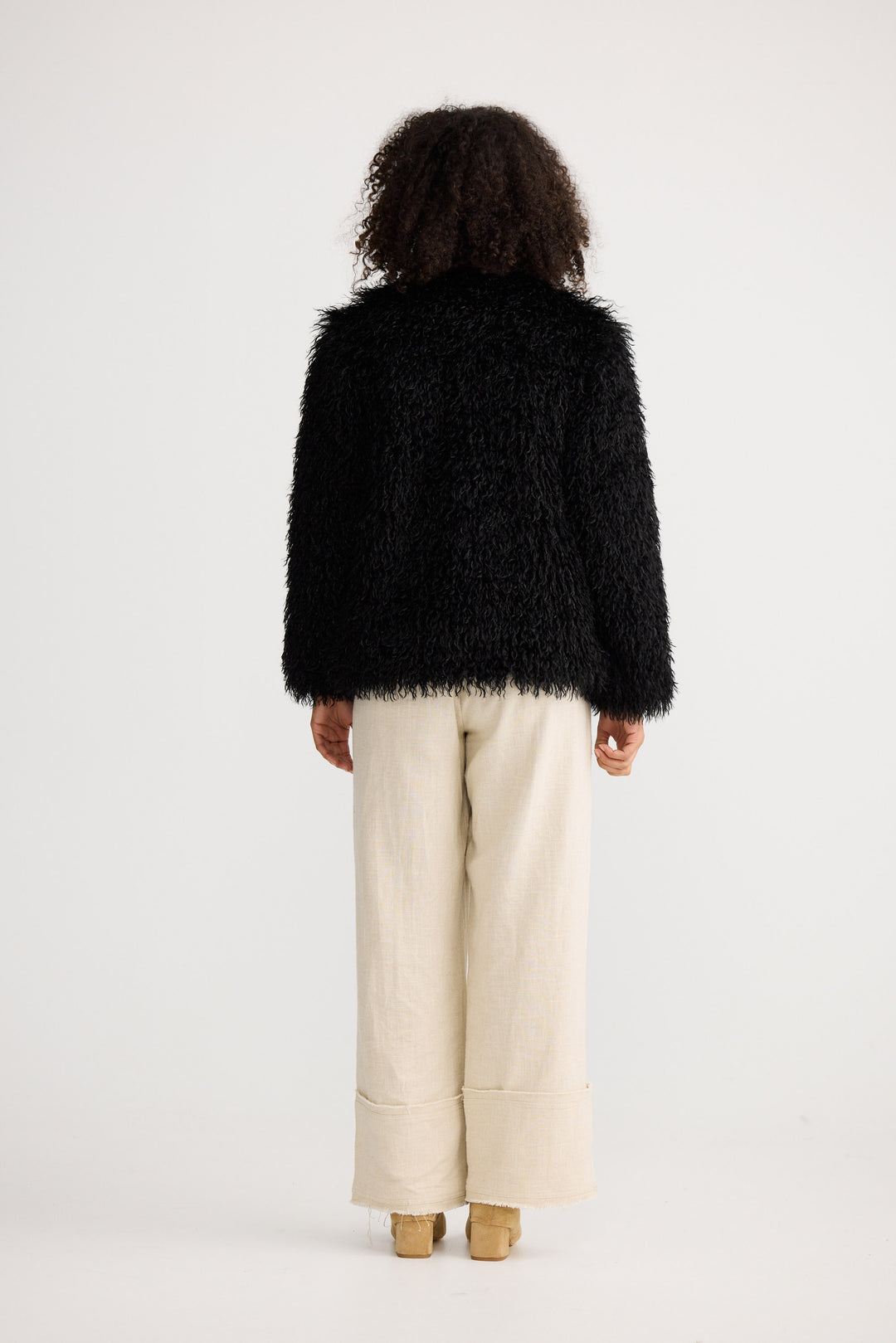 Person wearing a black fluffy jacket and beige pants on a white background