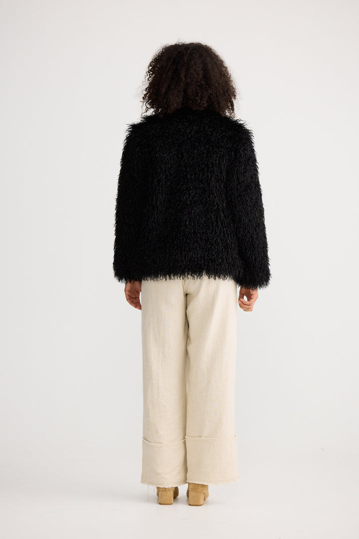 Person wearing a black fluffy jacket and beige pants on a white background
