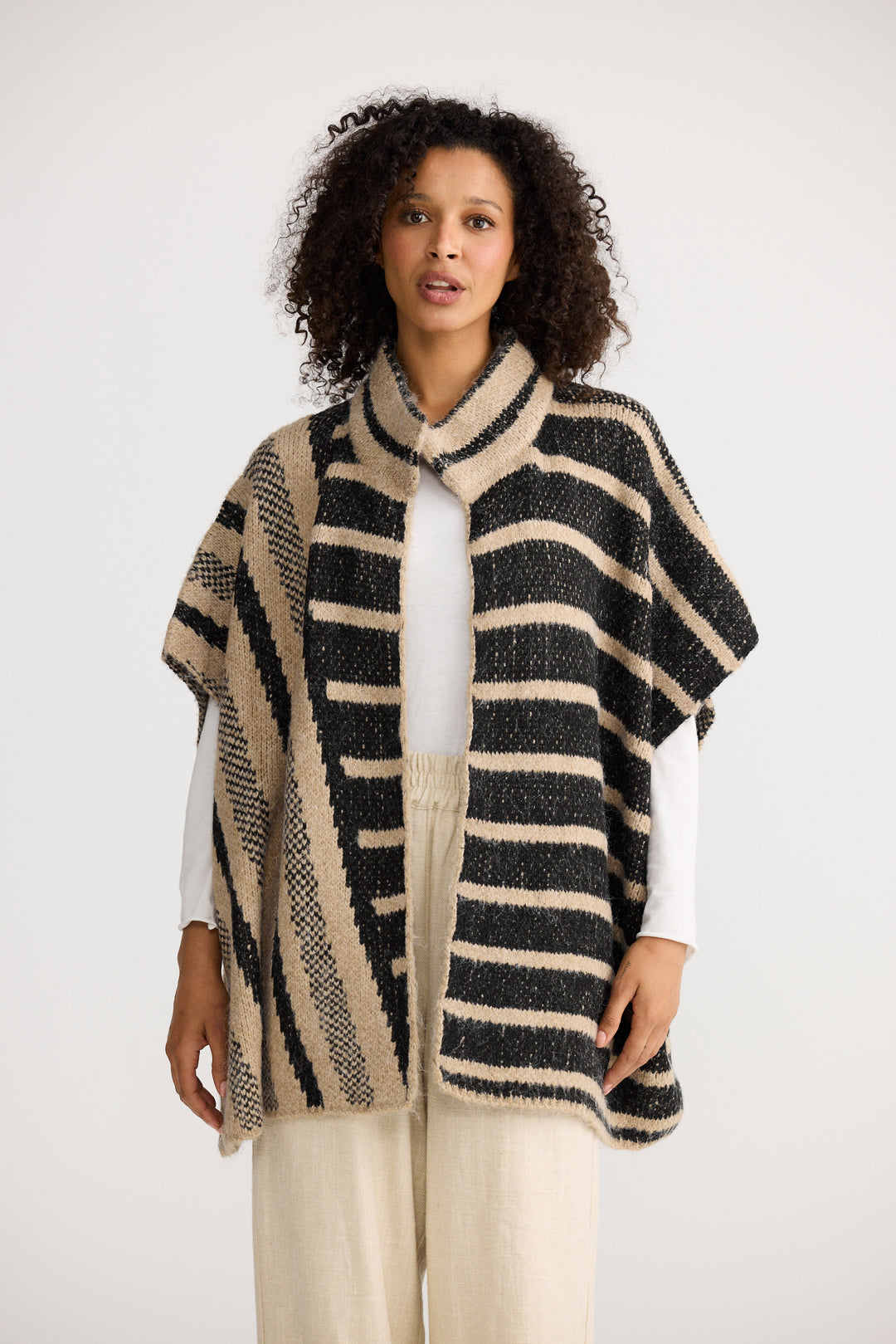 Woman wearing a black and beige striped poncho on a white background