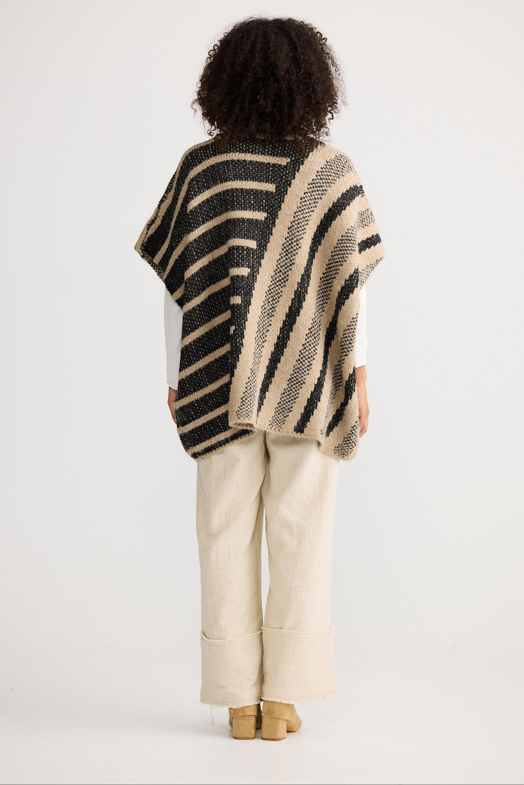 Person wearing a striped poncho and beige pants on a white background