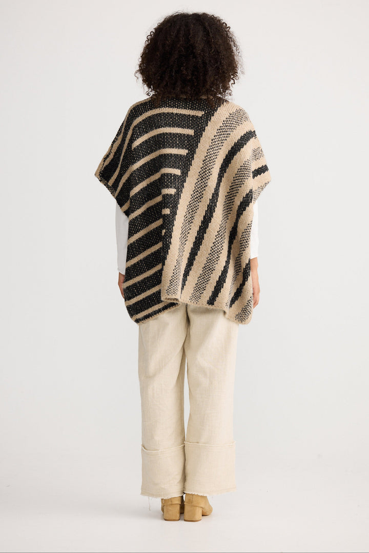 Person wearing a striped poncho and beige pants on a white background