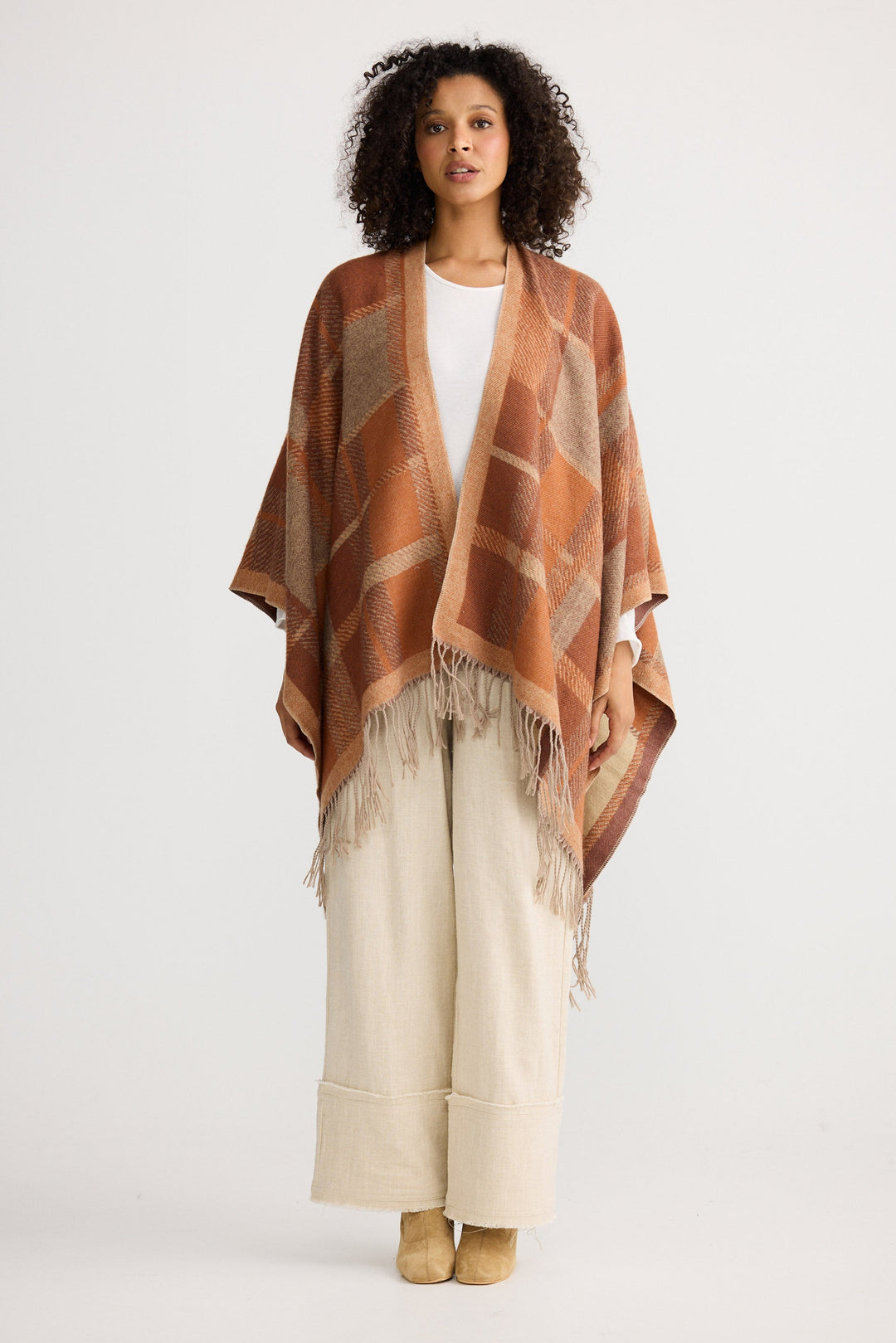 Woman wearing a patterned shawl over a white top and beige pants on a white background