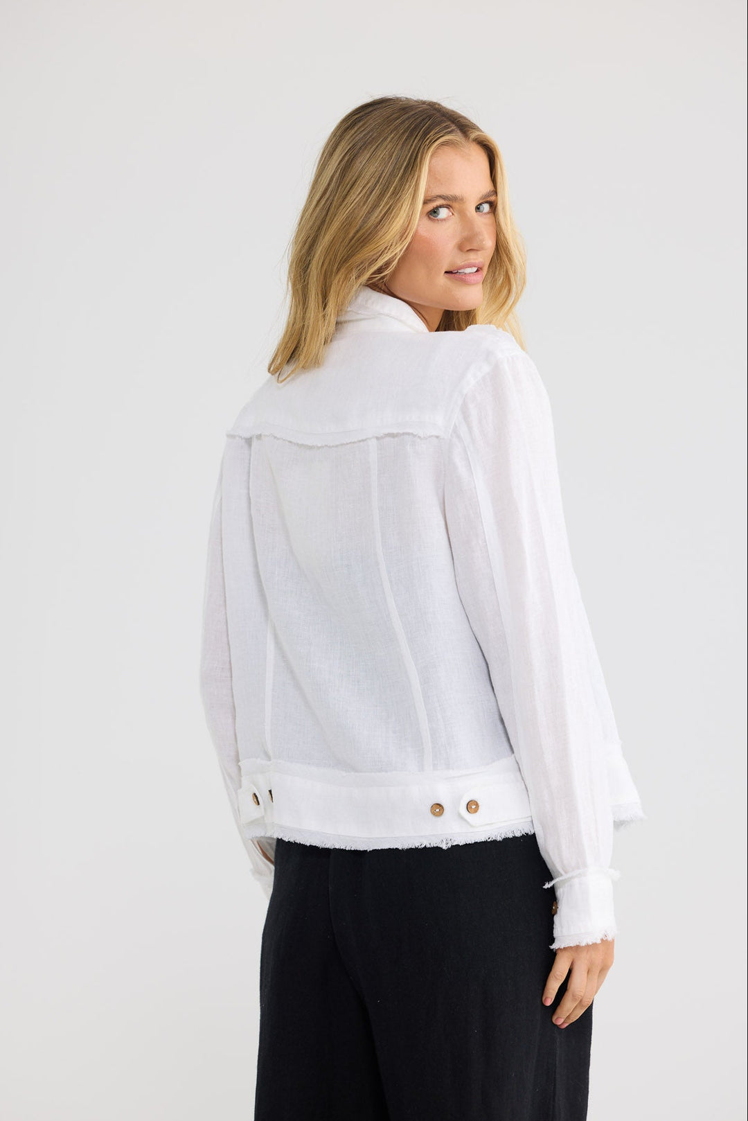 A woman wearing a white long-sleeve jacket with a wide collar and raw-edge hem, shown from the back against a light gray studio background.