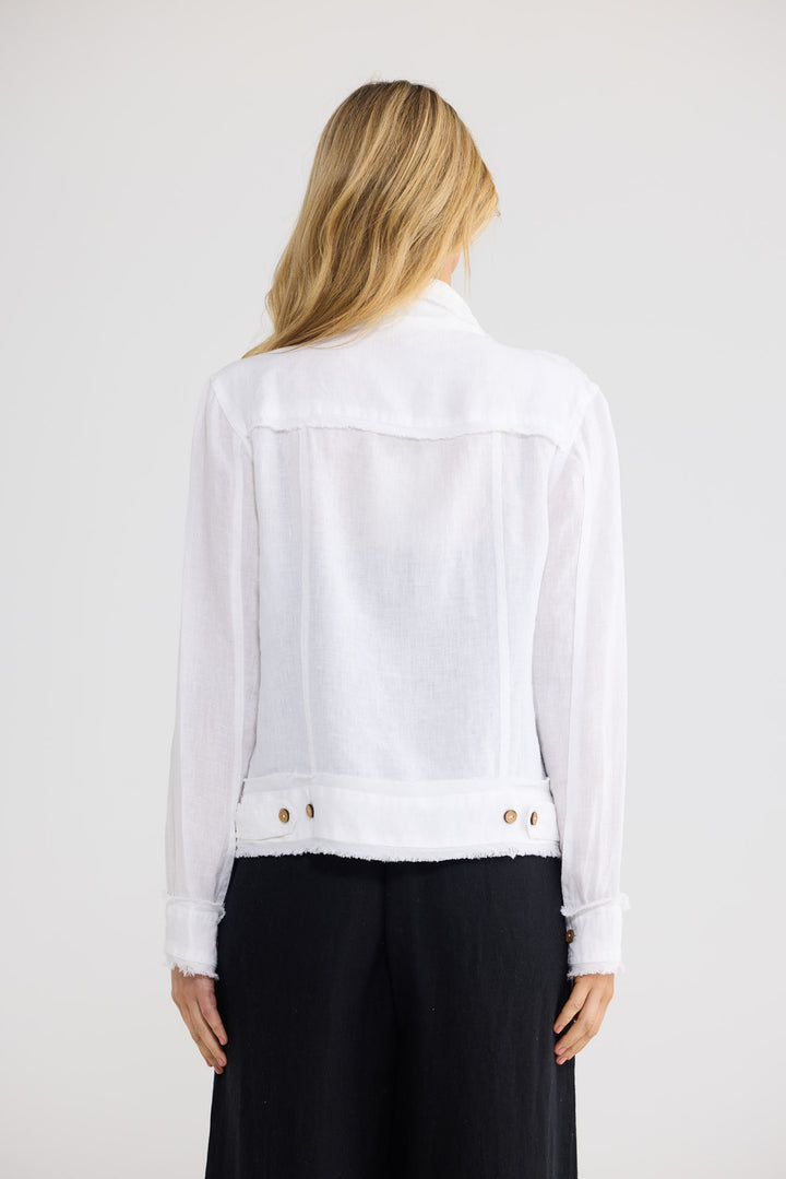 A woman viewed from the back wearing a white long-sleeve cropped jacket with a raw hem and gold-tone buttons, paired with black pants, against a light gray studio background.